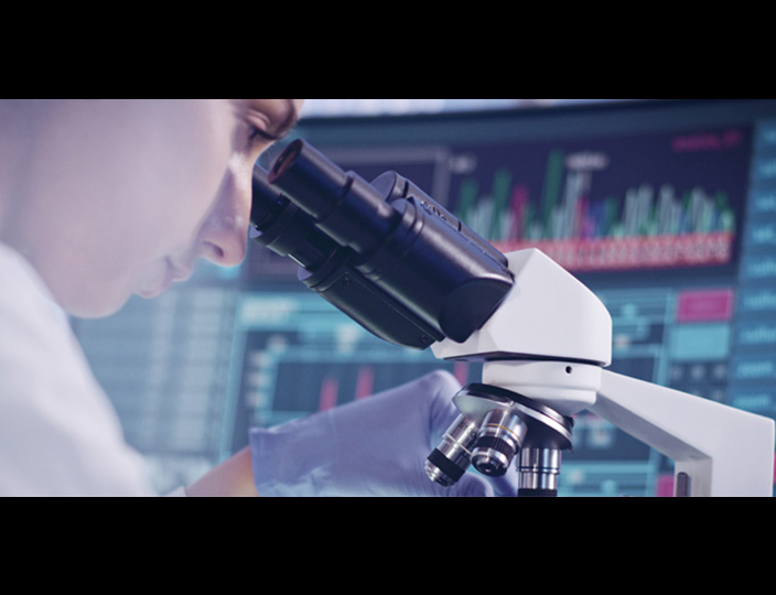 A scientist looks through the eyepiece of a binocular microscope.